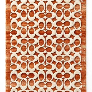 May include: A rectangular area rug featuring a repeating cream-colored C-shaped logo pattern set against a textured, burnt orange background. The rug has a thick, tufted pile construction with a consistent, symmetrical design throughout the surface.