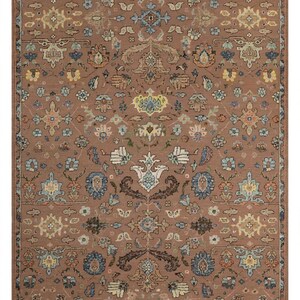 May include: A rectangular area rug featuring a dusty rose background with a symmetrical pattern of floral and botanical motifs in shades of light blue, cream, yellow, and dark brown, finished with a thin border in a matching rose tone.