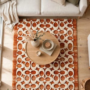 May include: A wool high-low hand tufted rug in light burnt orange abrash with a repeating cream-colored Signature C pattern. The rug measures 5x8 ft and features a textured surface with raised, looped pile details throughout the design.