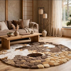 May include: A large circular area rug featuring a textured, pebble-like pattern in various shades of brown, tan, cream, and white. The rug is composed of raised, rounded tufted sections that mimic the appearance of smooth river stones on a floor.