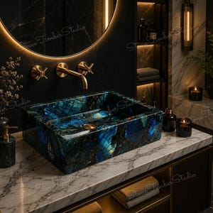 May include: A rectangular bathroom sink crafted from polished blue labradorite stone with iridescent highlights, featuring a gold-toned drain, mounted on a white marble countertop with a gold-toned wall-mounted faucet and cross-handle controls.