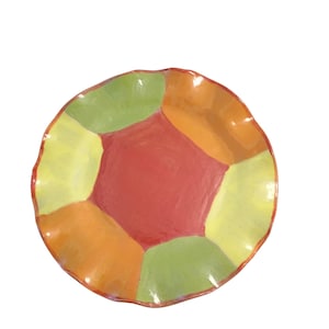 May include: A round ceramic plate with a wavy, uneven rim. The surface features a geometric pattern of six segments in alternating colors of red, lime green, and orange, with a central red hexagon surrounded by five trapezoidal sections.