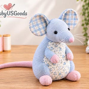 May include: A stuffed mouse toy made of blue fabric with a floral patterned belly, pink paws, and a long pink tail. The ears feature a blue and white plaid pattern. The mouse has black bead eyes, a pink nose, and white thread whiskers. Text reads ArtsbyUSGoods.