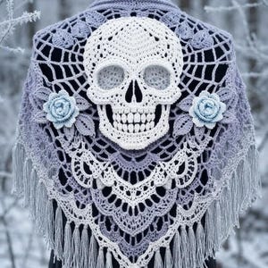 May include: A triangular crochet shawl in shades of light purple and white, featuring a large central white skull motif, two light blue crocheted roses on either side, a spiderweb-inspired lace pattern, and long fringe along the bottom edges.