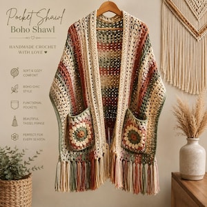 May include: A crochet shawl featuring a multi-colored striped pattern in shades of cream, sage green, and rust orange. The garment includes two square granny-style pockets on the front and a long, decorative tassel fringe along the bottom hem.