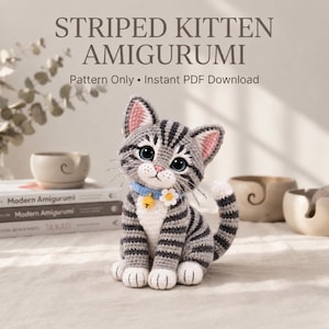 Pode incluir: Um amigurumi de gatinho de crochê com listras cinzas e brancas, olhos grandes e escuros, nariz rosa e bigodes longos. O gatinho usa uma coleira azul clara com um pequeno sino amarelo e uma flor branca. O texto diz: STRIPED KITTEN AMIGURUMI.