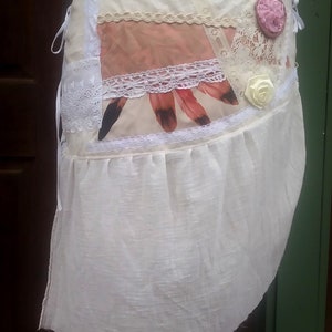 May include: A white skirt with a layered design featuring lace, fabric, and floral embellishments. The skirt has a ruffled hem and is tied at the waist.