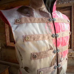 May include: A sleeveless vest with a floral pattern in shades of pink, brown, and white. The vest has multiple straps with decorative metal buckles.