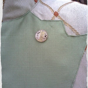May include: A close-up of a green fabric with a decorative gold button. The button has a floral design.