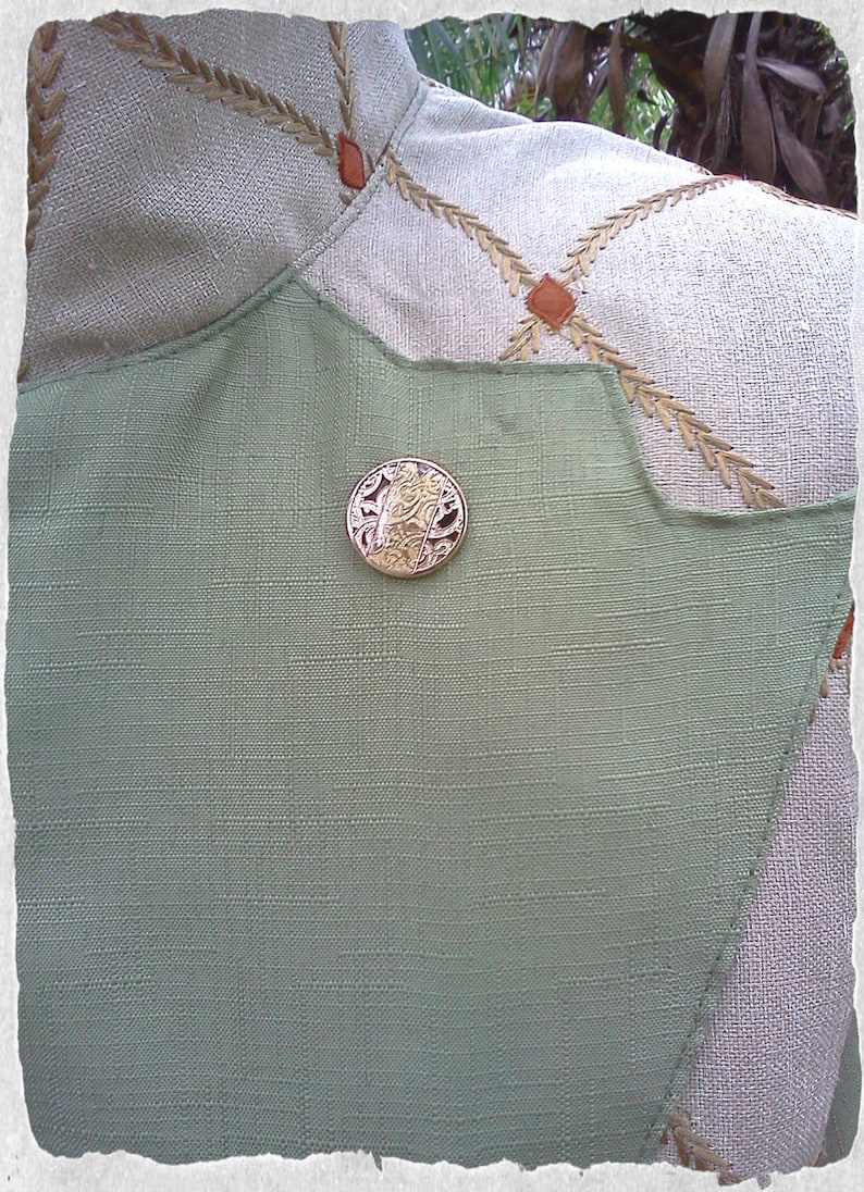 May include: A close-up of a green fabric with a decorative gold button. The button has a floral design.