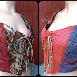 May include: A red, brown, and blue patchwork corset with a lace-up front and gold eyelets. The corset has a paisley pattern on one side and a striped pattern on the other.