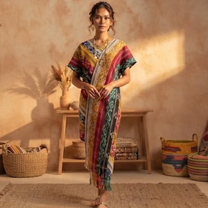 Op de afbeelding: Een mouwloze, kuitlange tuniekjurk met een levendig, veelkleurig ikat-patroon met verticale strepen in rood, geel, groen en zwart. Het kledingstuk heeft een V-hals, een ontspannen silhouet en een gefranjerde zoom aan de onderkant.