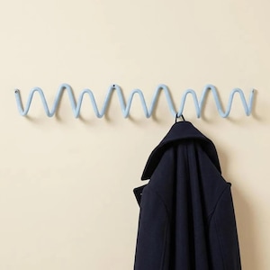 Peut inclure: Un porte-manteau mural bleu clair doté d'un design en fil métallique ondulé ou en zigzag continu et répétitif. Un manteau bleu marine foncé est suspendu à l'une des sections incurvées du porte-manteau, fixé au mur aux deux extrémités.