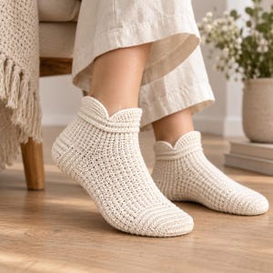 May include: A pair of off-white ankle socks crafted with a textured crochet knit pattern. The socks feature a reinforced toe area and a distinctive scalloped edge detail around the cuff, providing a structured fit that sits just above the ankle bone.