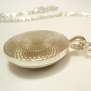 Op de afbeelding: Zilveren ketting met hanger met een ronde, getextureerde zilveren hanger. De hanger heeft een cirkelvormig ontwerp met een verhoogd midden.