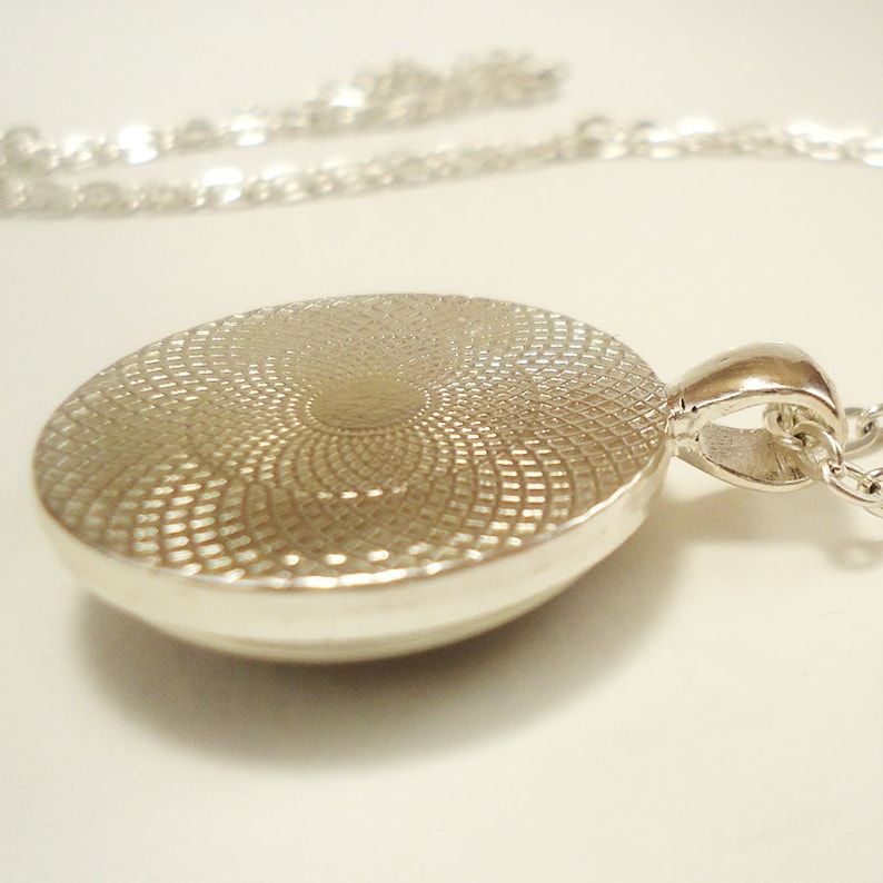 Op de afbeelding: Zilveren ketting met hanger met een ronde, getextureerde zilveren hanger. De hanger heeft een cirkelvormig ontwerp met een verhoogd midden.