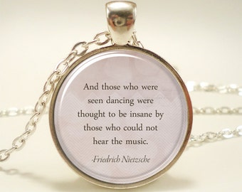 Op de afbeelding: Zilveren ketting met een ronde glazen hanger met een citaat van Friedrich Nietzsche: "En degenen die dansten, werden voor gek verklaard door degenen die de muziek niet konden horen."