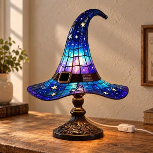 May include: A stained glass table lamp shaped like a pointed wizard hat. The shade features a blue and purple celestial pattern with white stars and a dark band with a rectangular buckle. It sits on a decorative dark metal base with a cord.