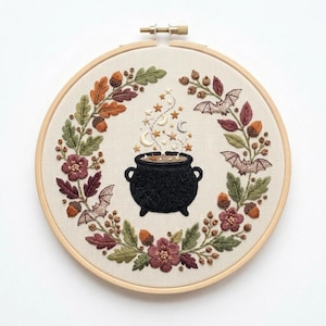 Peut inclure: Un tambour à broder circulaire contenant un tissu crème avec un motif brodé à la main représentant un chaudron noir au centre d'une couronne de feuilles d'automne, de glands, de fleurs et de trois petites chauves-souris.