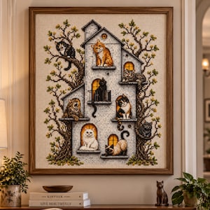 May include: A framed cross-stitch embroidery depicting a multi-storey house structure integrated into a large tree. Various cats in orange, black, white, and calico patterns occupy the windows, balconies, and branches of the tree-house design.