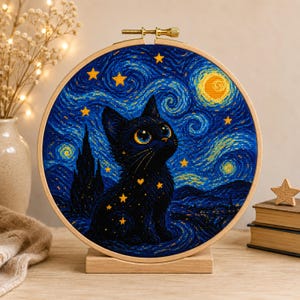 Puede incluir: Un bastidor de bordado circular de madera que contiene una pieza de punto de cruz con un gato negro sentado frente a un cielo nocturno azul oscuro con remolinos, estrellas amarillas y una luna amarilla brillante, sobre un soporte de madera.