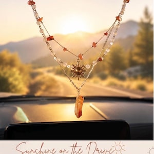 May include: A layered car charm featuring gold-toned chains, clear and orange-hued stone beads, a central sun-shaped metal pendant, and a dangling raw orange crystal point. The text reads: Sunshine on the Drive, Layered Car Charm, Light, Positivity, Protection.