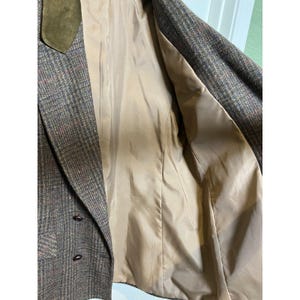 May include: A brown tweed blazer featuring a multi-colored plaid pattern, a solid olive green velvet collar, and two dark brown buttons on the front. The interior is fully lined with a smooth, solid tan fabric, showing the inner construction.