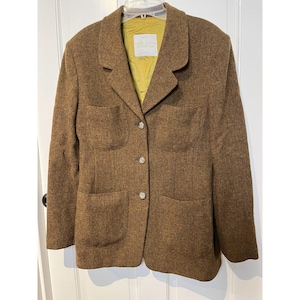 May include: A brown tweed blazer featuring a notched lapel, three front buttons, and four patch pockets. The interior is lined with a solid olive green fabric and includes a white label with the text United Colors of Benetton.