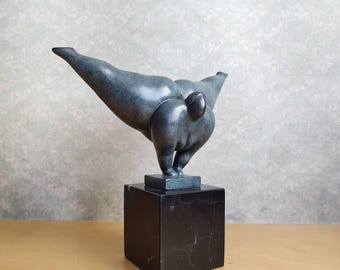 May include: A dark blue-grey abstract sculpture of a figure in a dynamic, forward-leaning pose with outstretched limbs. The figure is mounted on a smooth, square, black marble base, creating a solid foundation for the curved, metallic-looking form.