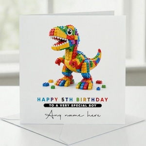 May include: A square greeting card featuring a colorful dinosaur constructed from plastic building blocks. The text reads: HAPPY 5TH BIRTHDAY TO A VERY SPECIAL BOY. Below this, the phrase Any name here is printed in a black script font.