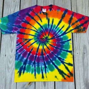Może przedstawiać: Koszulka tie-dye z wzorem spiralnym w odcieniach ż&oacute;łtego, pomarańczowego, czerwonego, fioletowego, niebieskiego i zielonego. Koszulka ma czarne tło.