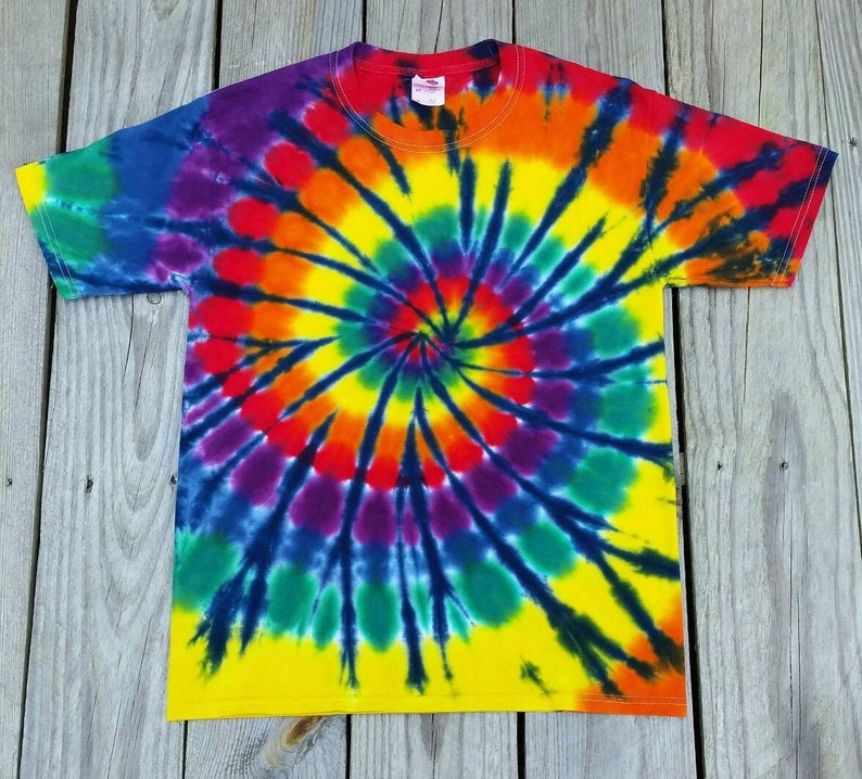 Może przedstawiać: Koszulka tie-dye z wzorem spiralnym w odcieniach ż&oacute;łtego, pomarańczowego, czerwonego, fioletowego, niebieskiego i zielonego. Koszulka ma czarne tło.