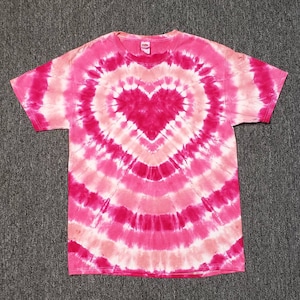 Pu&ograve; includere: T-shirt tie-dye rosa e bianca con un grande disegno a forma di cuore rosa al centro.