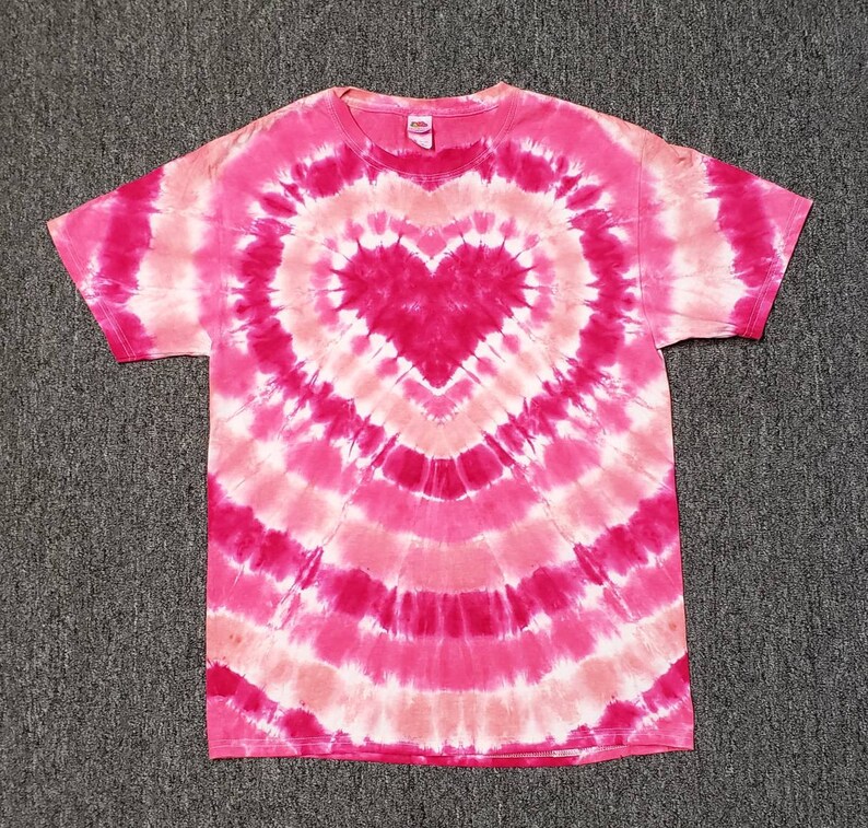 Pu&ograve; includere: T-shirt tie-dye rosa e bianca con un grande disegno a forma di cuore rosa al centro.