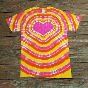 May include: A tie-dye t-shirt with a heart design in shades of pink, orange, and yellow. The heart is surrounded by concentric circles of the same colors.