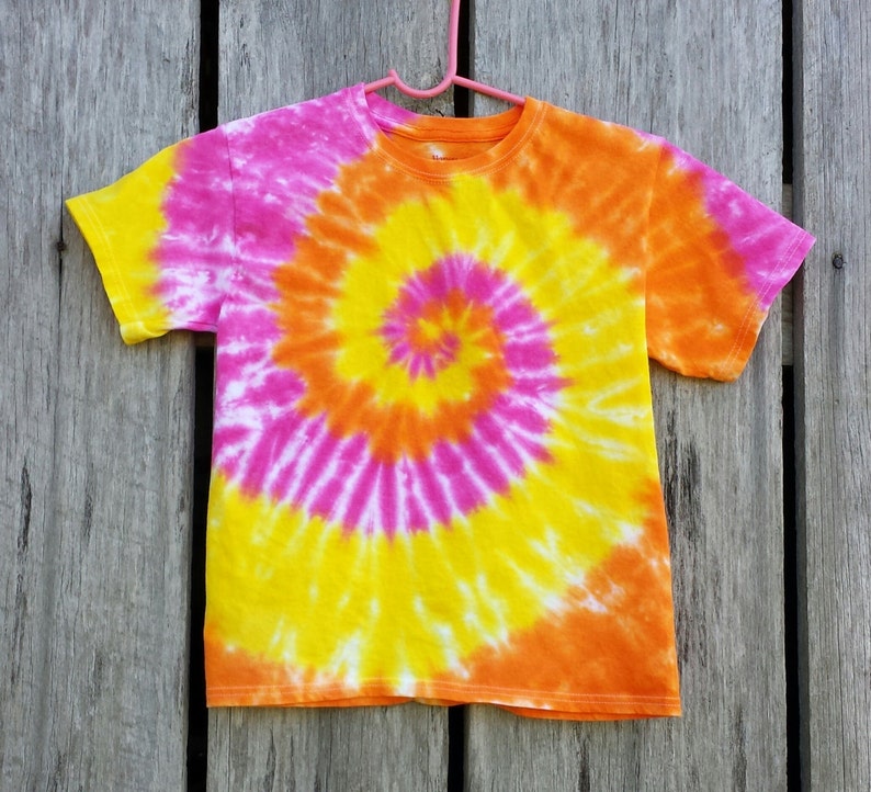 May include: A tie-dye t-shirt with a spiral pattern in shades of pink, yellow, and orange.