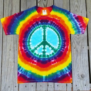 May include: A tie-dye t-shirt with a peace sign in the center. The shirt is a rainbow of colors, including red, orange, yellow, green, blue, indigo, and violet.