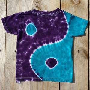 May include: A purple and teal tie-dye t-shirt with a yin yang design.