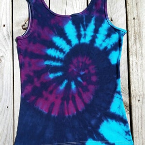 Pu&ograve; includere: Un top nero senza maniche con un motivo tie-dye in tonalit&agrave; di blu, viola e nero. Il motivo &egrave; un design a spirale.