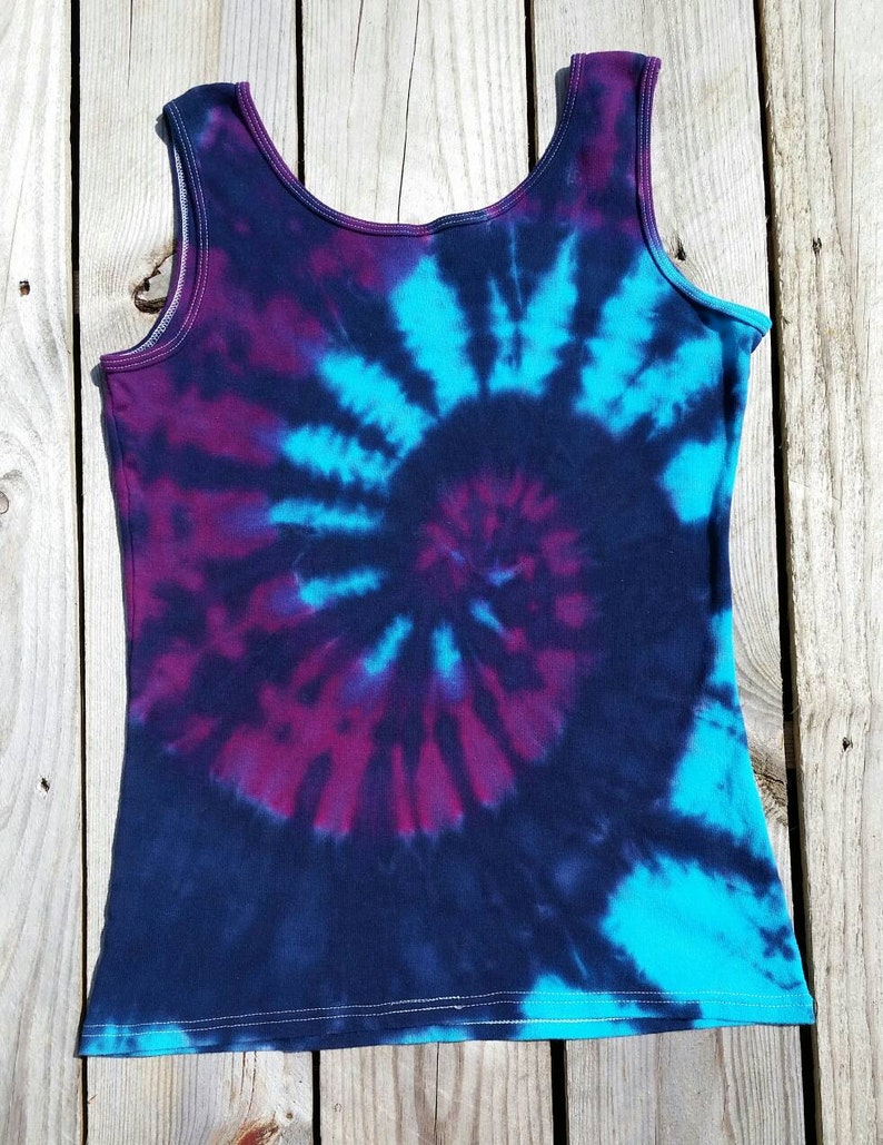 Pu&ograve; includere: Un top nero senza maniche con un motivo tie-dye in tonalit&agrave; di blu, viola e nero. Il motivo &egrave; un design a spirale.