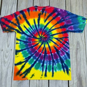 Może przedstawiać: Koszulka tie-dye z wzorem spiralnym w odcieniach czerwieni, pomarańczy, ż&oacute;łci, zieleni, błękitu, fioletu i czerni.