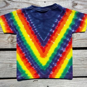 May include: A tie-dye t-shirt with a rainbow chevron pattern in shades of yellow, orange, red, green, blue, and purple. The shirt is made of a soft, comfortable cotton.