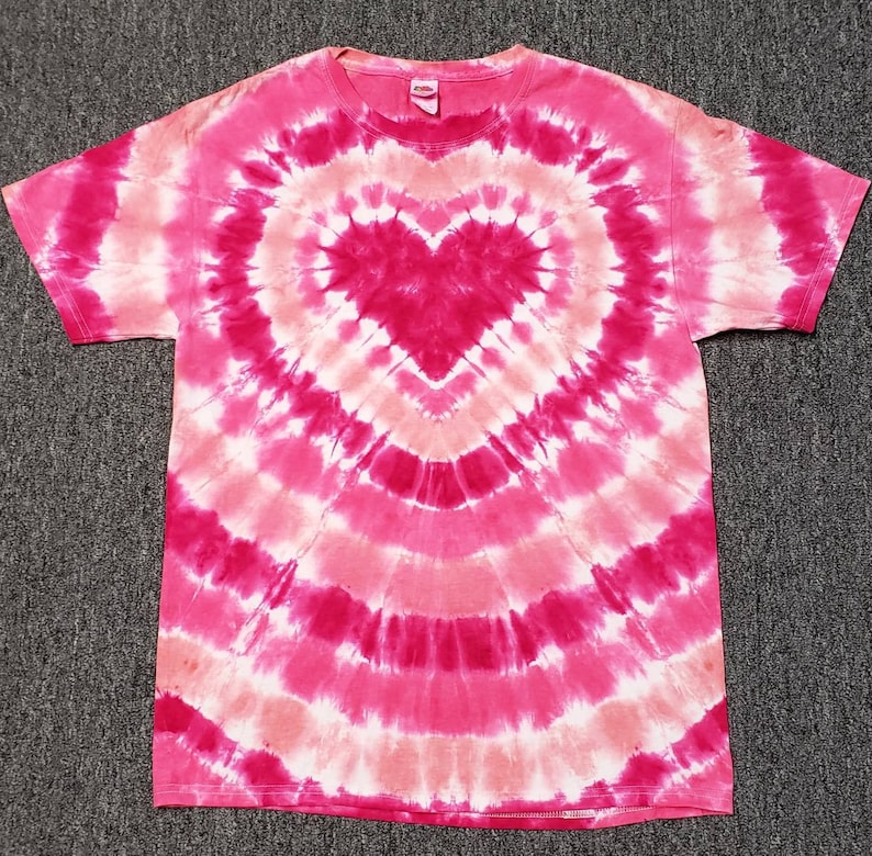 Pu&ograve; includere: Una maglietta tie-dye rosa e bianca con una grande forma di cuore al centro. Il cuore &egrave; di un rosa pi&ugrave; scuro.