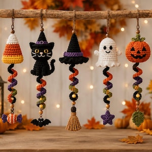 May include: Five hanging crochet ornaments featuring a candy corn, a black cat with a witch hat, a witch hat, a white ghost, and an orange pumpkin. Each ornament has a colorful spiral tail ending in a small charm like a candy, bat, broom, star, or leaf.