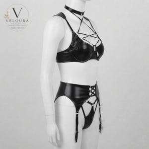 May include: A black faux leather lingerie set featuring a bra with a choker collar, crisscross straps, and silver-tone metal rings. The high-waisted garter belt includes lace-up detailing and attached garter straps, creating a structured appearance.