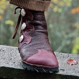 Puede incluir: Un par de botas de cuero marrón con hebillas plateadas decorativas. Las botas tienen una punta puntiaguda y una suela gruesa.