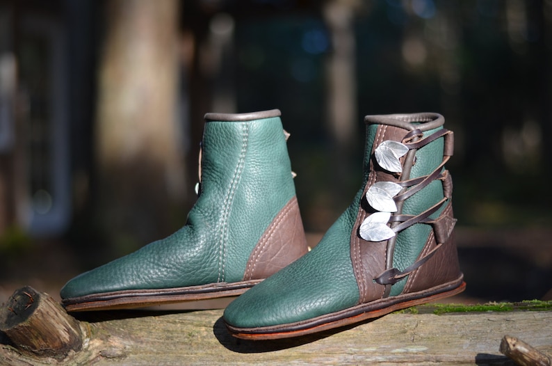 May include: A pair of green leather boots with brown leather accents and silver leaf embellishments on the laces.