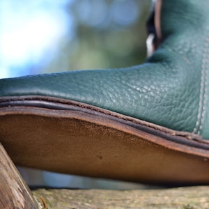 May include: Close-up of the sole of a green leather boot with a brown leather heel. The boot is resting on a piece of wood.