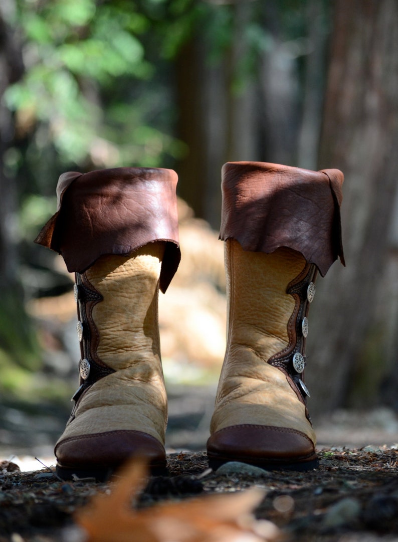 May include: A pair of brown leather boots with decorative silver buttons. The boots have a tan colored shaft and a brown leather toe.