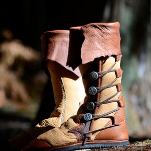 May include: A pair of brown leather boots with decorative metal buckles and laces. The boots are worn and have a distressed look.
